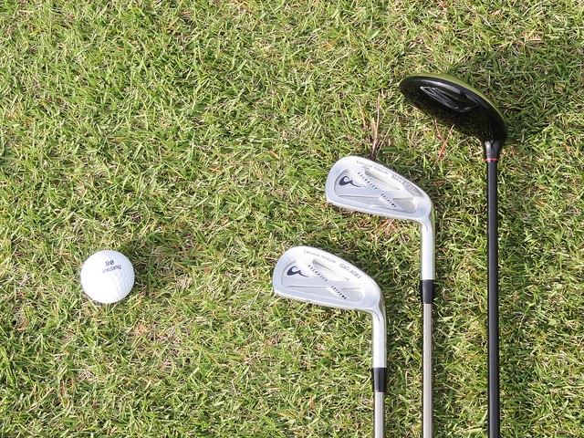 3 golf clubs lying on the grass next to golf ball